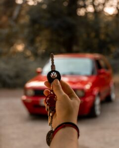 une personne tenant une clé de voiture devant une voiture rouge